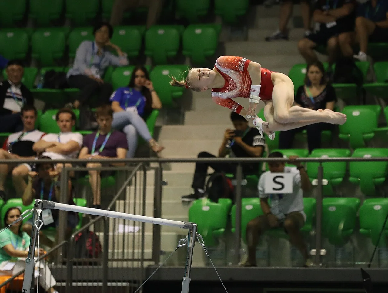 Gymnaste en action aux barres asymétriques lors d’une compétition junior